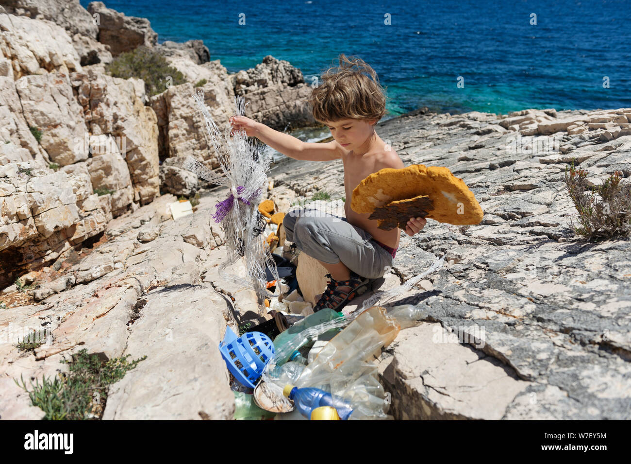 Petit garçon le nettoyage de plage plein de bouteilles en plastique rigide et d'autres ordures emportées sur la côte. Banque D'Images