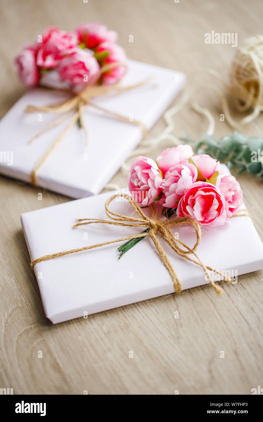 Boîte cadeau de style naturel fabriquée à la main sur une table en bois. Boîte cadeau faite à la main, enveloppée de papier blanc. Éléments de décoration à motifs floraux. Banque D'Images