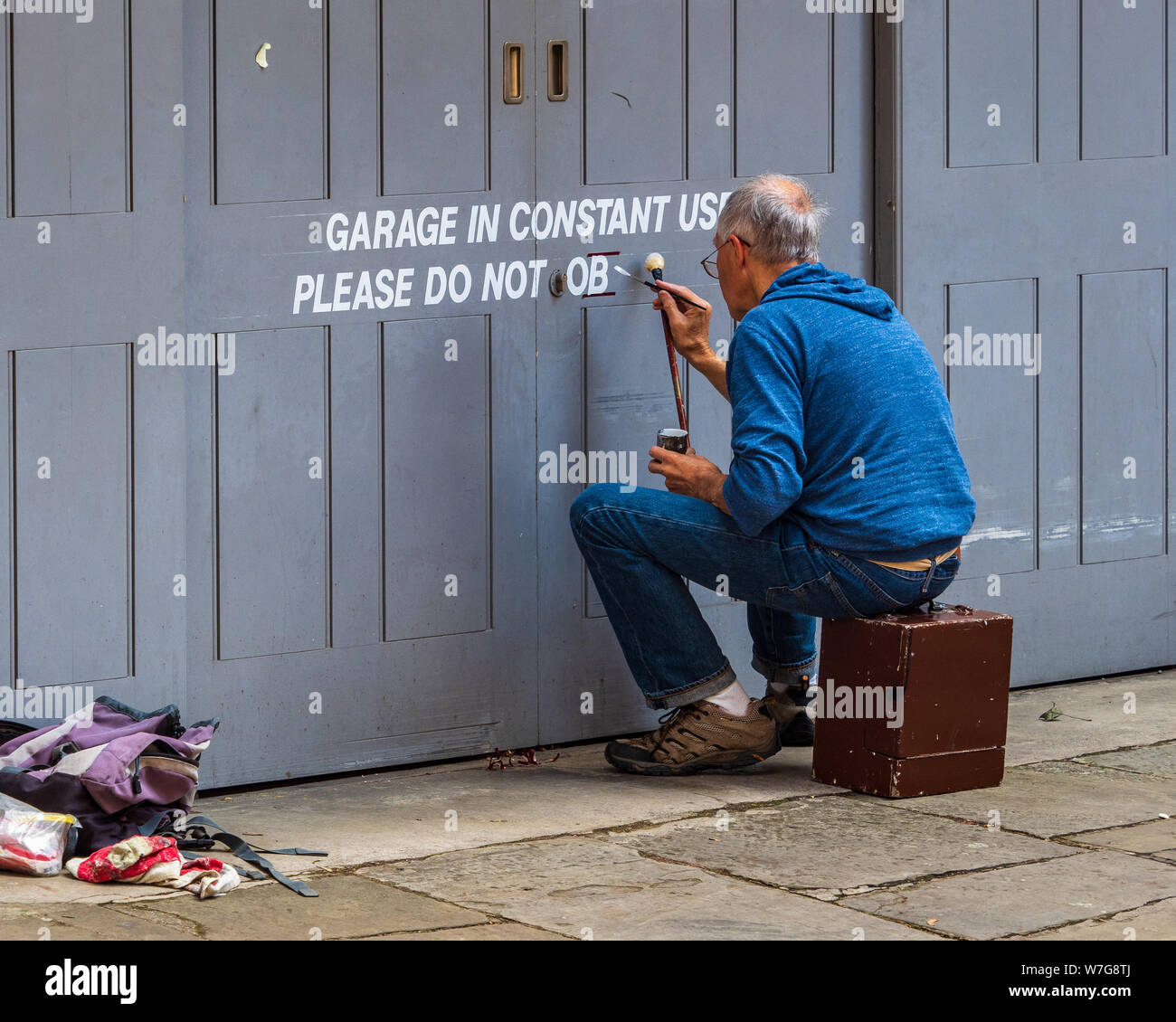 Peintre d'affiche au travail. Inscrivez-peinture sur une porte de garage dans le centre de Cambridge UK - Garage en utilisation constante Banque D'Images