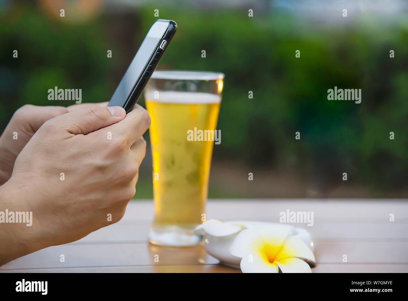 L'homme à l'aide de mobile pendant l'happy time vous détendre au restaurant avec boisson et vert jardin contexte - les gens se détendre avec la technologie concept de vie Banque D'Images