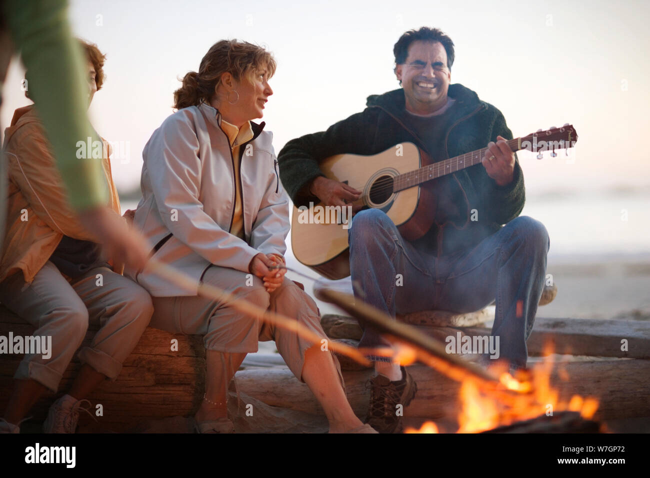 Famille assis autour d'un feu de camp et les guimauves grillage playing guitar Banque D'Images