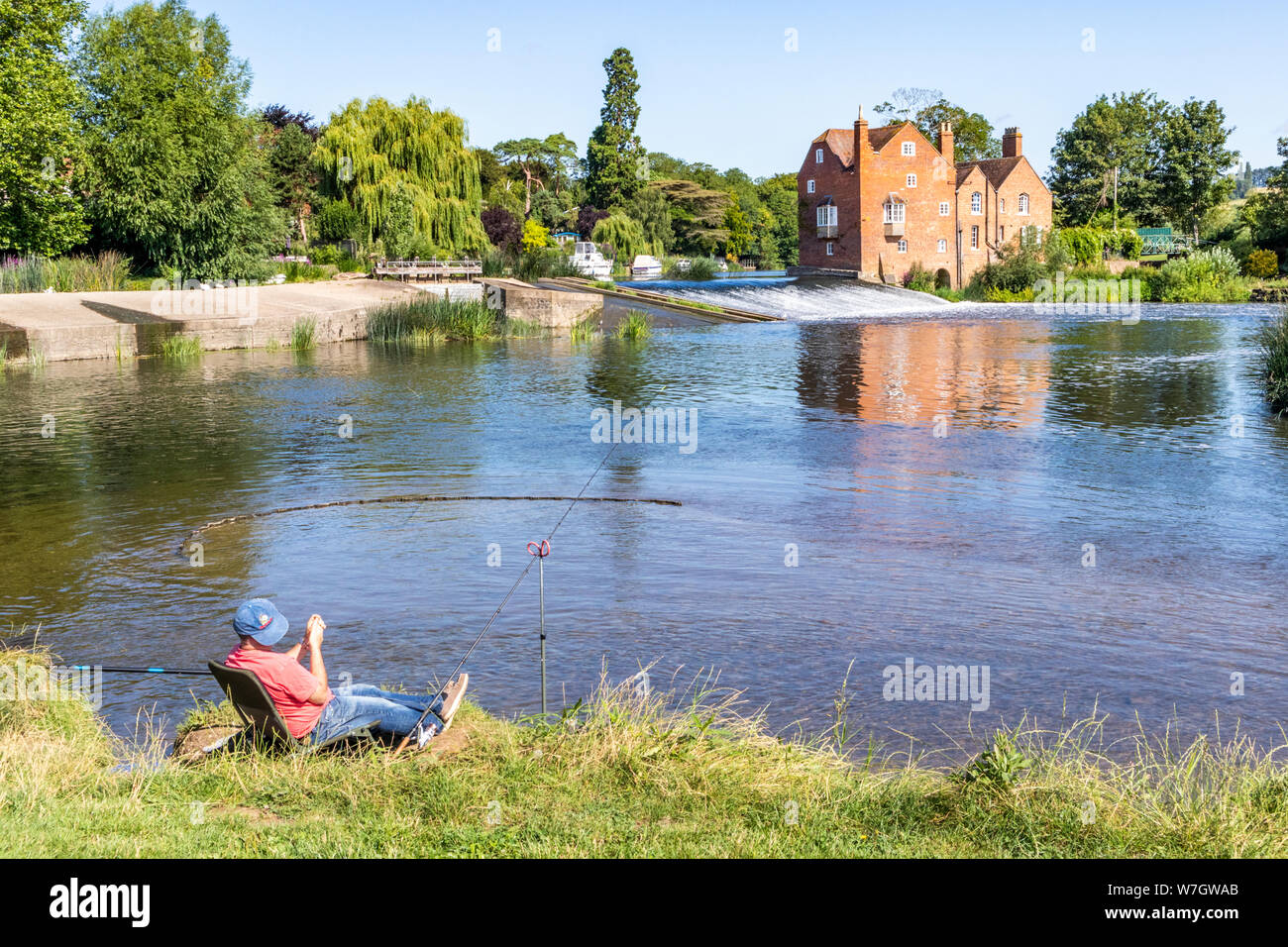 Soleil matinal sur Cropthorne Mill et un pêcheur au bord de la rivière Avon à Fladbury Worcestershire, Royaume-Uni Banque D'Images