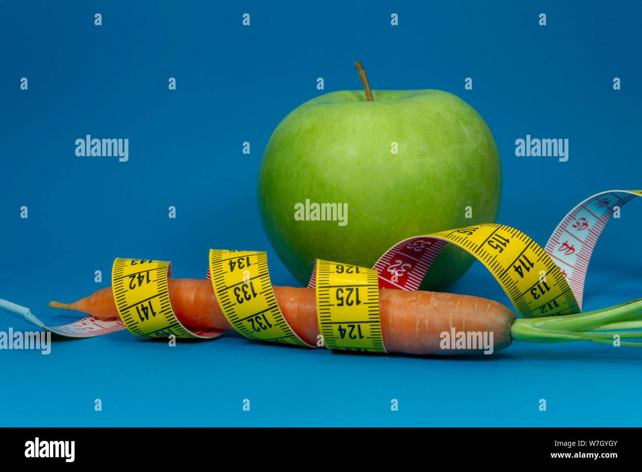 La perte de poids et régime alimentaire sain concept avec un ruban à mesurer, de carotte et de pomme verte sur fond bleu Banque D'Images