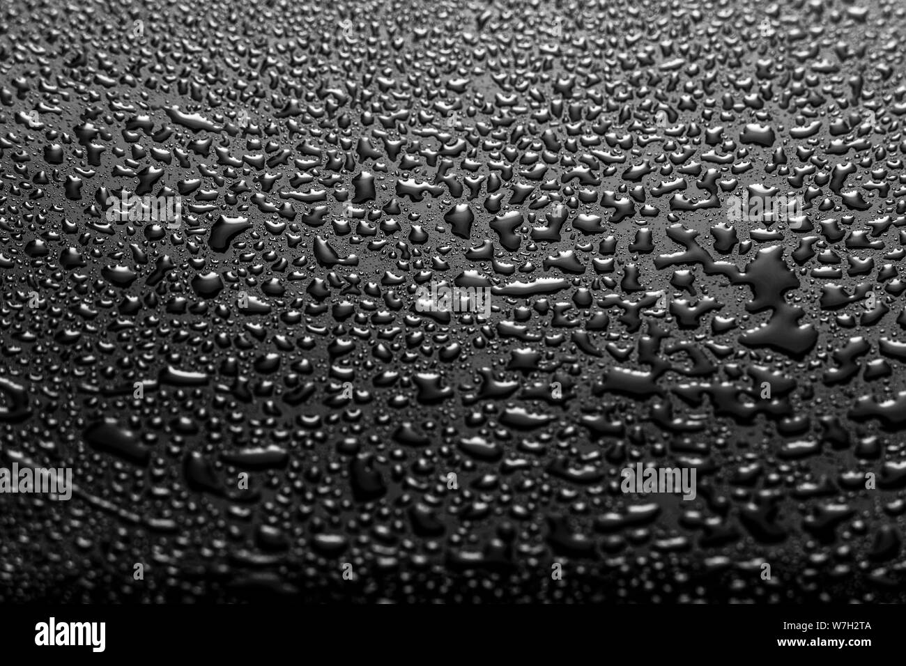 Les gouttes d'eau brillant sur un verre foncé. Goutte d'eau sur une surface noire. Banque D'Images