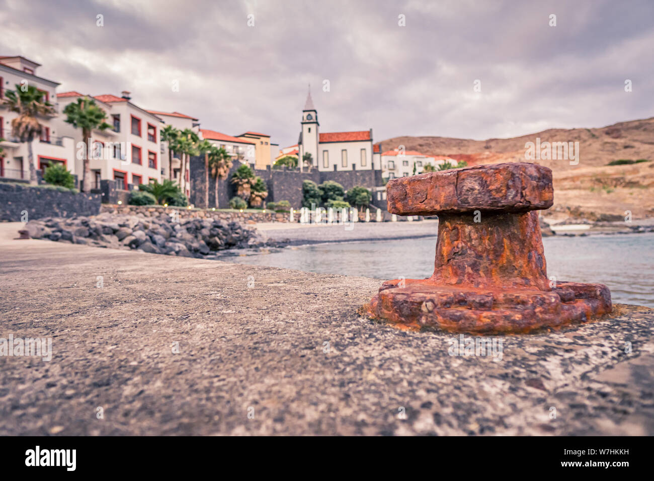 OLd rusty bollard sur un quai en pierre avec village floues en arrière-plan Banque D'Images