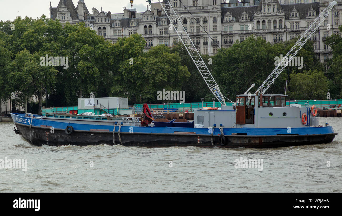 Un bateau de travail avec sauts et grands conteneurs remplis de déchets va en amont sur la Tamise à Londres, un samedi après-midi en août. Banque D'Images