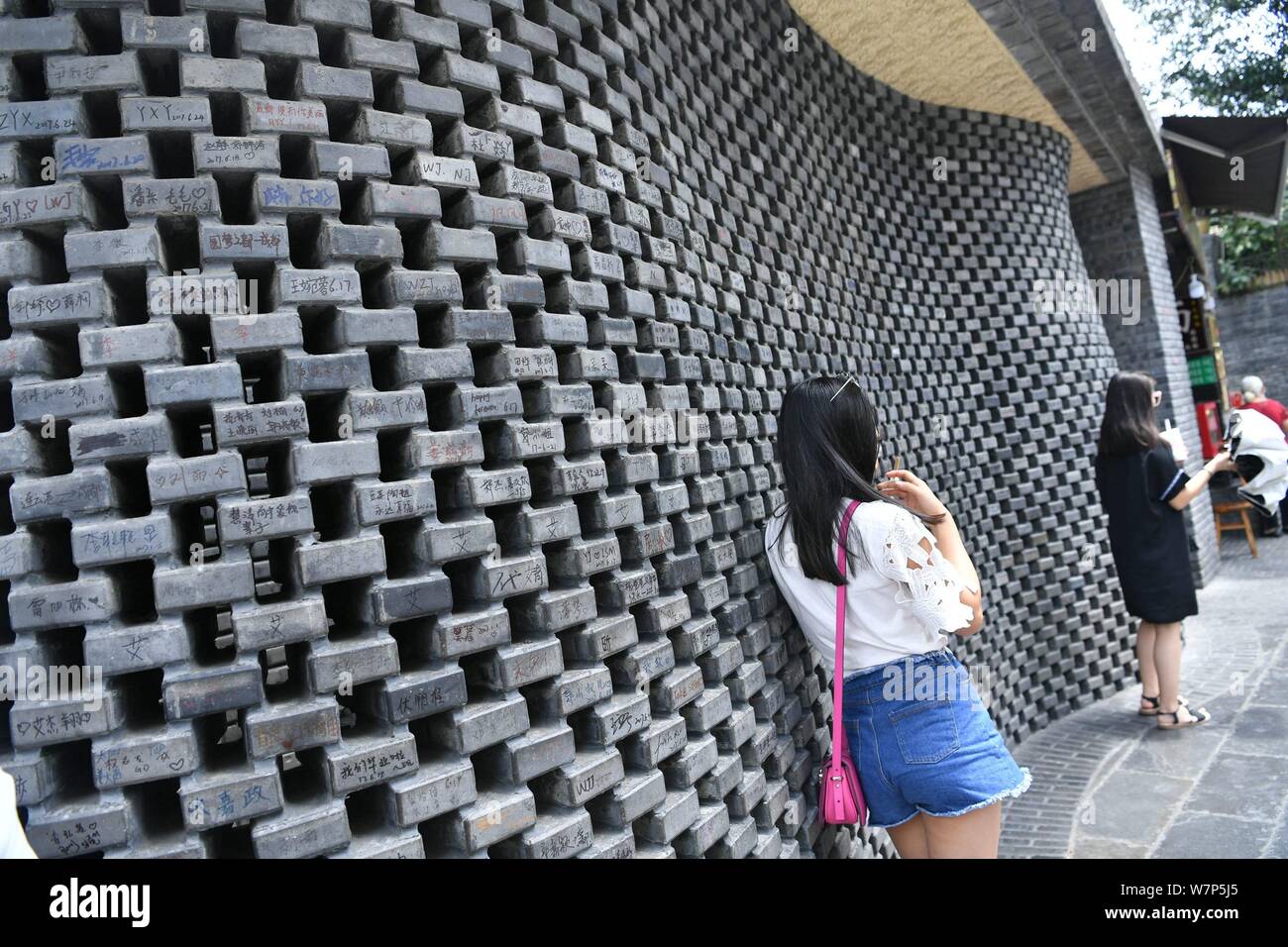 Les touristes de prendre des photos avec un sol carrelé mur recouvert de graffitis dans la région de Kuan Zhai Alley, un célèbre site culturel qui relève de la protection de l'environnement, dans la ville de Chengdu, Banque D'Images