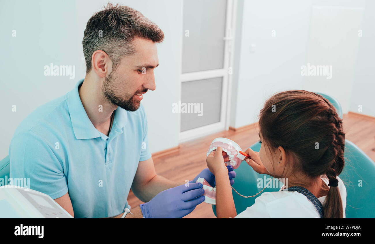 Enseignement dentiste peu mixed race girl se brosser les dents à l'aide de dents humaines modèle à une clinique dentaire Banque D'Images
