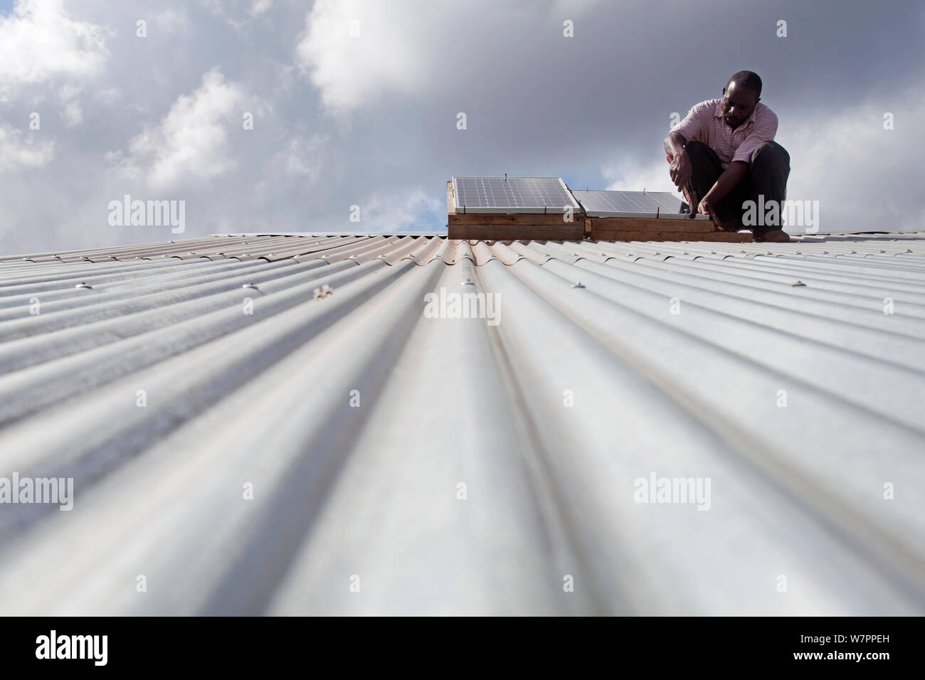 Fixation technicien panneau solaire sur un toit en tôle ondulée, Miono, région de la Tanzanie. Banque D'Images