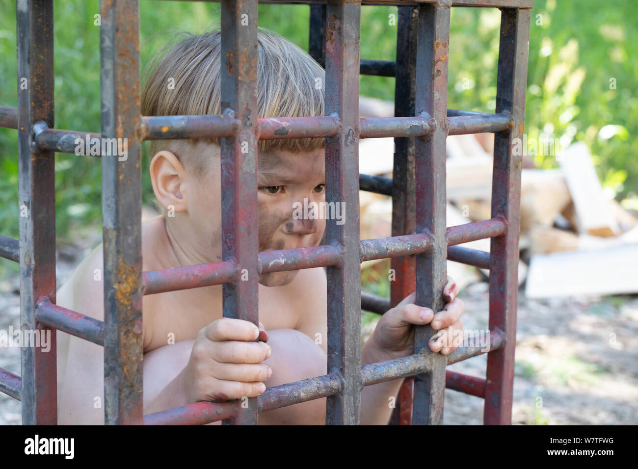 5-year-old boy à peau blanche avec des cheveux blonds sales et dénudé assis dans une cage. concept d'enlèvement, l'esclavage des enfants Banque D'Images
