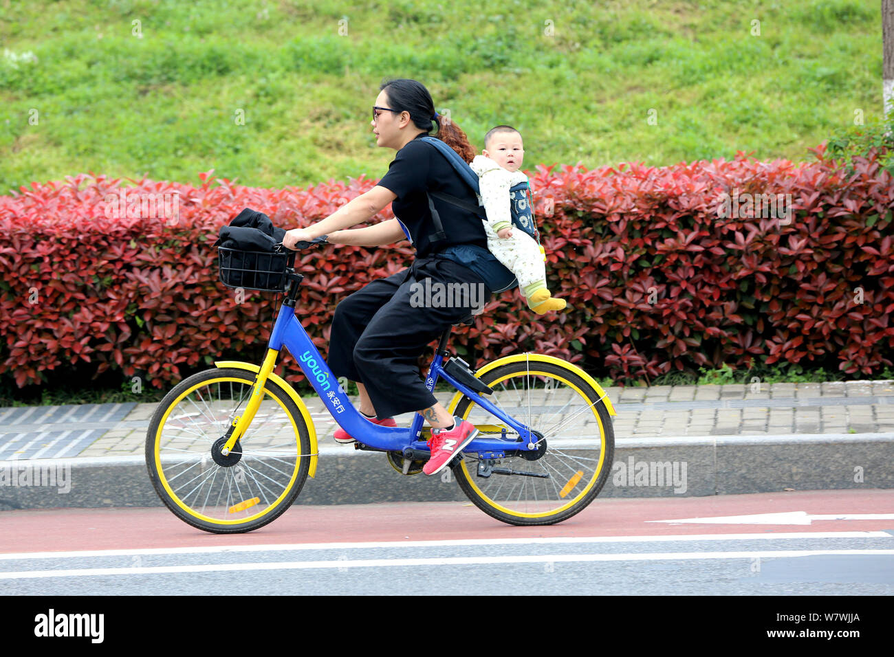 FILE--Une femme chinoise porte son bébé avec l'aide d'une écharpe porte-bébé  à faire de la bicyclette de Chinois de vélos en libre-service dans la ville  de Xiangfan, Ch central Photo Stock -
