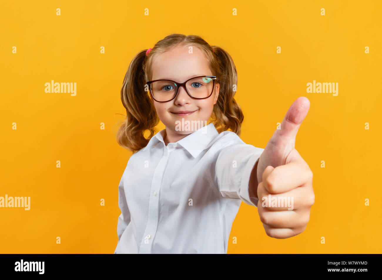 Portrait of a cute little girl attrayants dans des verres. Montre enfant pouce vers le haut sur un fond jaune. Banque D'Images