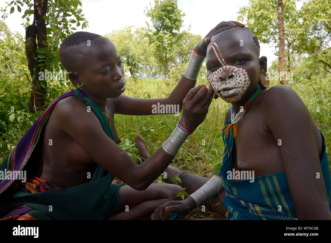 Les jeunes Suri / Surma woman painting une autre femme&# 39;s visage. La vallée de la rivière Omo, en Ethiopie, en septembre 2014. Banque D'Images