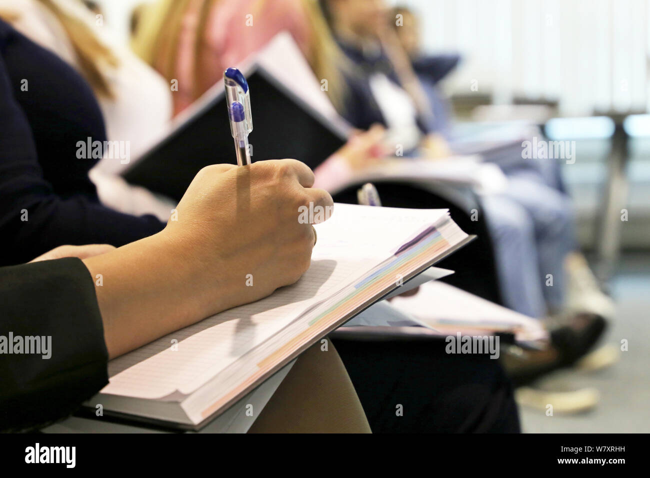 Les femmes assis dans une rangée dans une salle de conférence, femme la main avec pen écrit dans un bloc-notes. Concept de conférence, réunion d'affaires, cours au collège, les compétences Banque D'Images