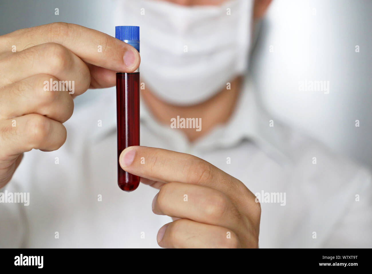 Tube à essai dans la main des hommes de près, dans l'homme masque médical tenant un flacon de liquide rouge. Concept de l'échantillon de sang, la recherche médicale, la vaccination Banque D'Images