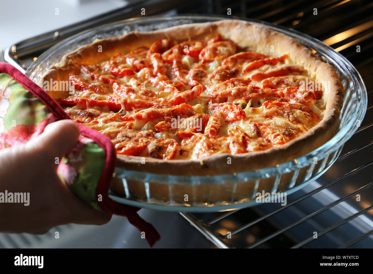 La cuisson de la pizza, la femme prend le gâteau fraîchement cuit au four avec du fromage, de la viande et les tomates de four électrique Banque D'Images