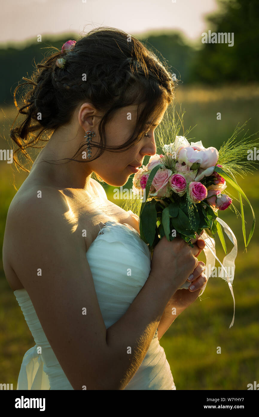 Jeune épouse dans l'odeur de profil son bouquet dans le coucher du soleil la lumière Banque D'Images