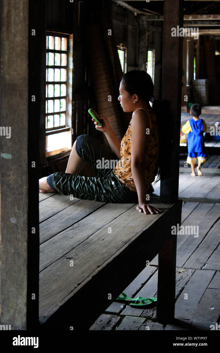 Femme Dayak sur téléphone mobile, dans la maison longue, Pontianka, l'ouest de Kalimantan, la partie indonésienne de Bornéo. Juin 2010. Banque D'Images