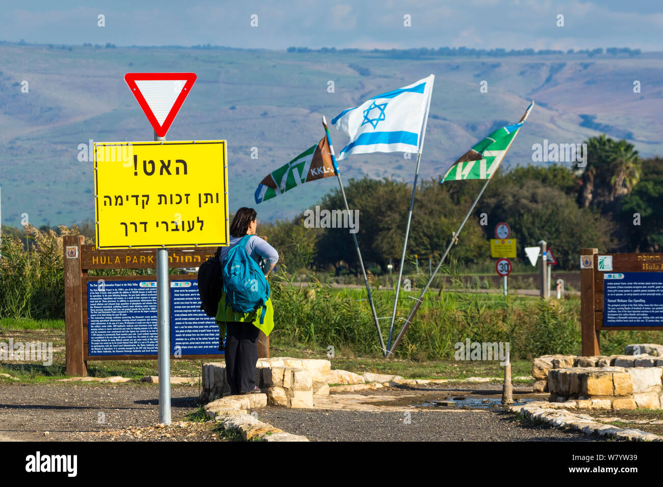 Panneau d'avertissement à ralentir, près de femme debout par des remontées de gaz méthane, avec drapeaux, Vallée de Hula, Israël, novembre 2014. Banque D'Images