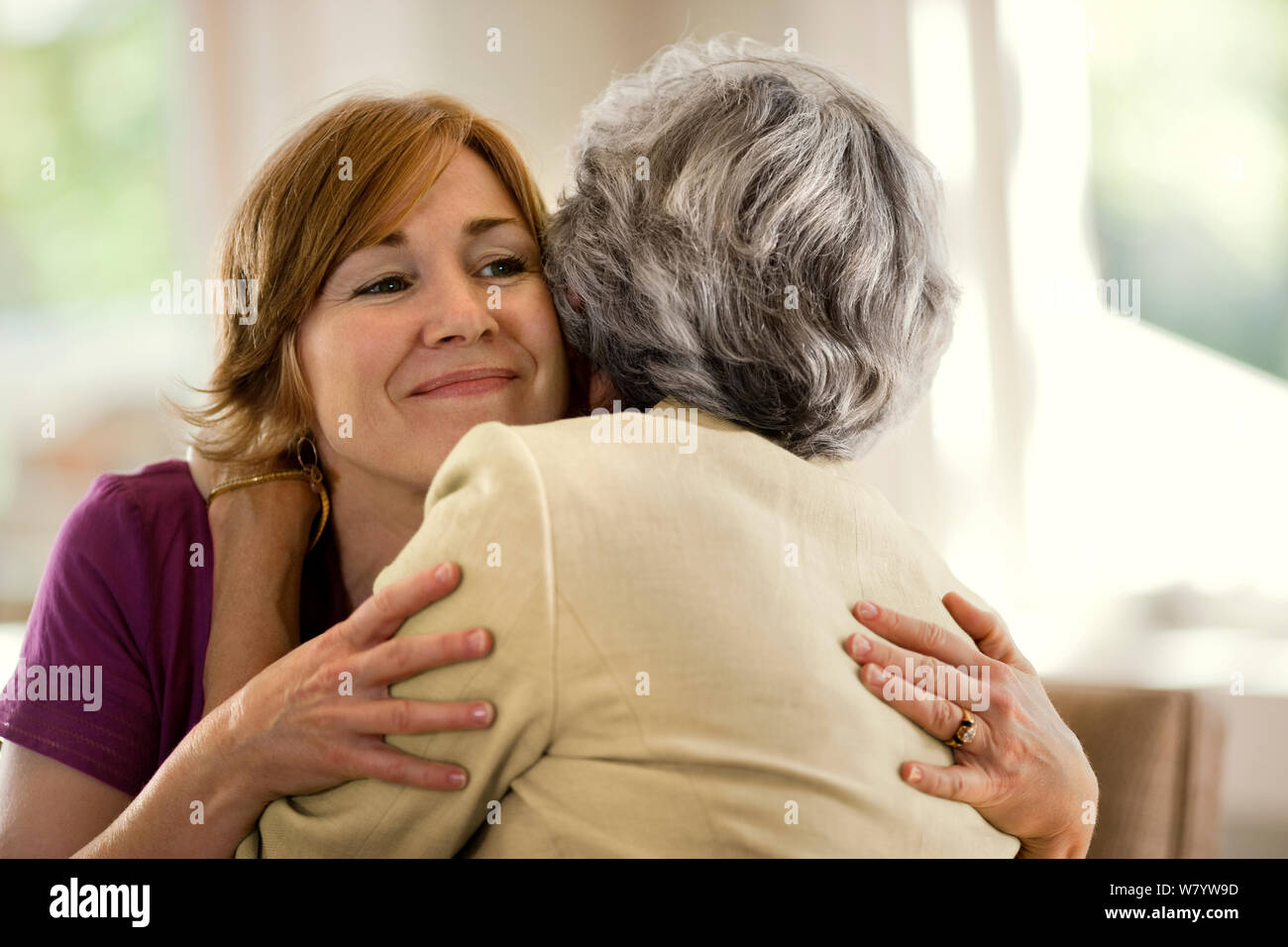 Jeune femme sourit avec une légère inquiétude qu'elle embrasse sa mère âgée. Banque D'Images