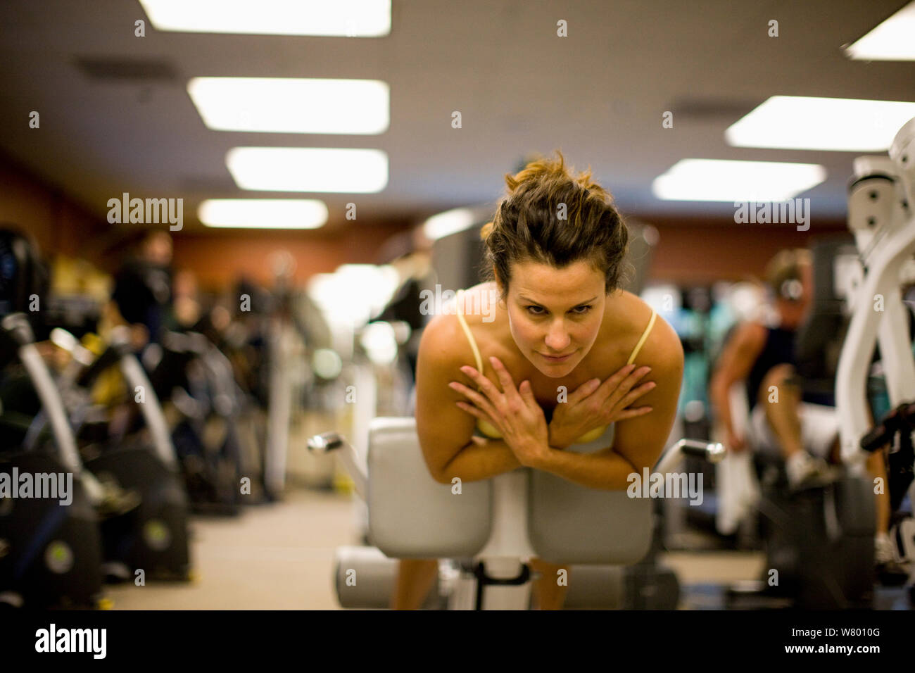Mid-adult woman working out sur une machine d'exercice avec ses mains croisées sur sa poitrine à l'intérieur d'une salle de sport. Banque D'Images