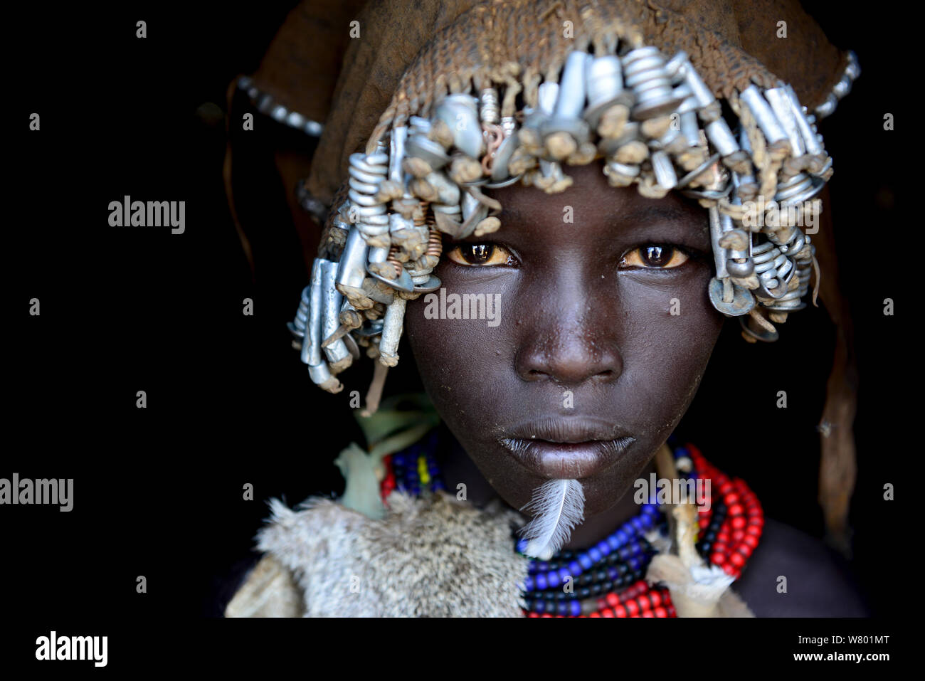 Dassanech fille avec coiffe de plumes d'écrous et boulons, et vers le bas sur le menton, tribu Dassanech, vallée de l'Omo. L'Éthiopie, Novembre 2014 Banque D'Images