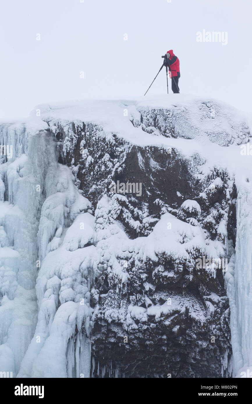 Photographe avec trépied sur le bord de Godafoss warterfall, gelé en hiver, l'Islande, février 2014. Banque D'Images