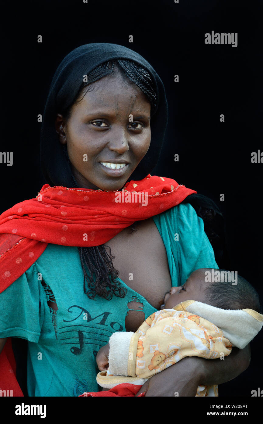 Loin femme avec tatouages / scarification de la peau sur son visage d'allaiter son bébé, dépression Danakil, région Afar, en Ethiopie, en mars 2015. Banque D'Images