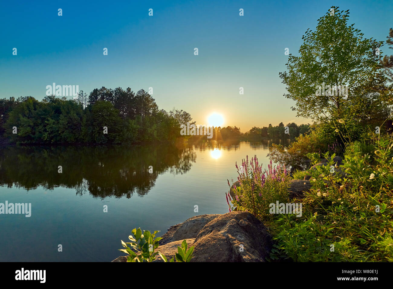 Coucher du soleil sur un lac avec l'eau et le ciel bleu, dans l'avant-plan la sauge et pierres rondes Banque D'Images