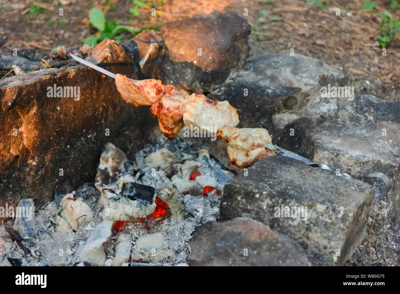 Shish kebab en brochettes est frit sur un brasero fait de pierres dans la forêt. Cuire la viande sur le feu vue d'en haut. Banque D'Images