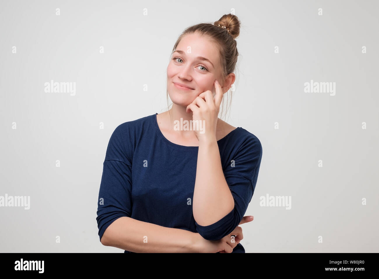 Happy young woman with hair in bun looking at camera avec joie et sourire charmeur. Banque D'Images