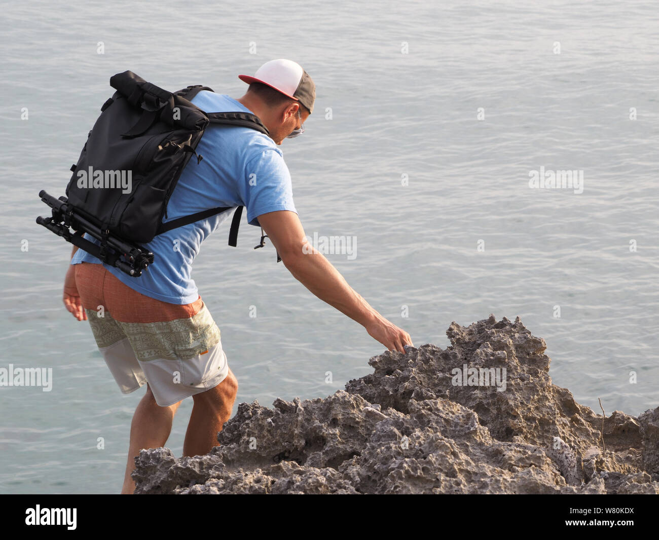 Un homme avec un sac à dos d'équipement photographique sur une plage de galets. vacances dans les Caraïbes. Vue de dos. L'océan Atlantique. Banque D'Images