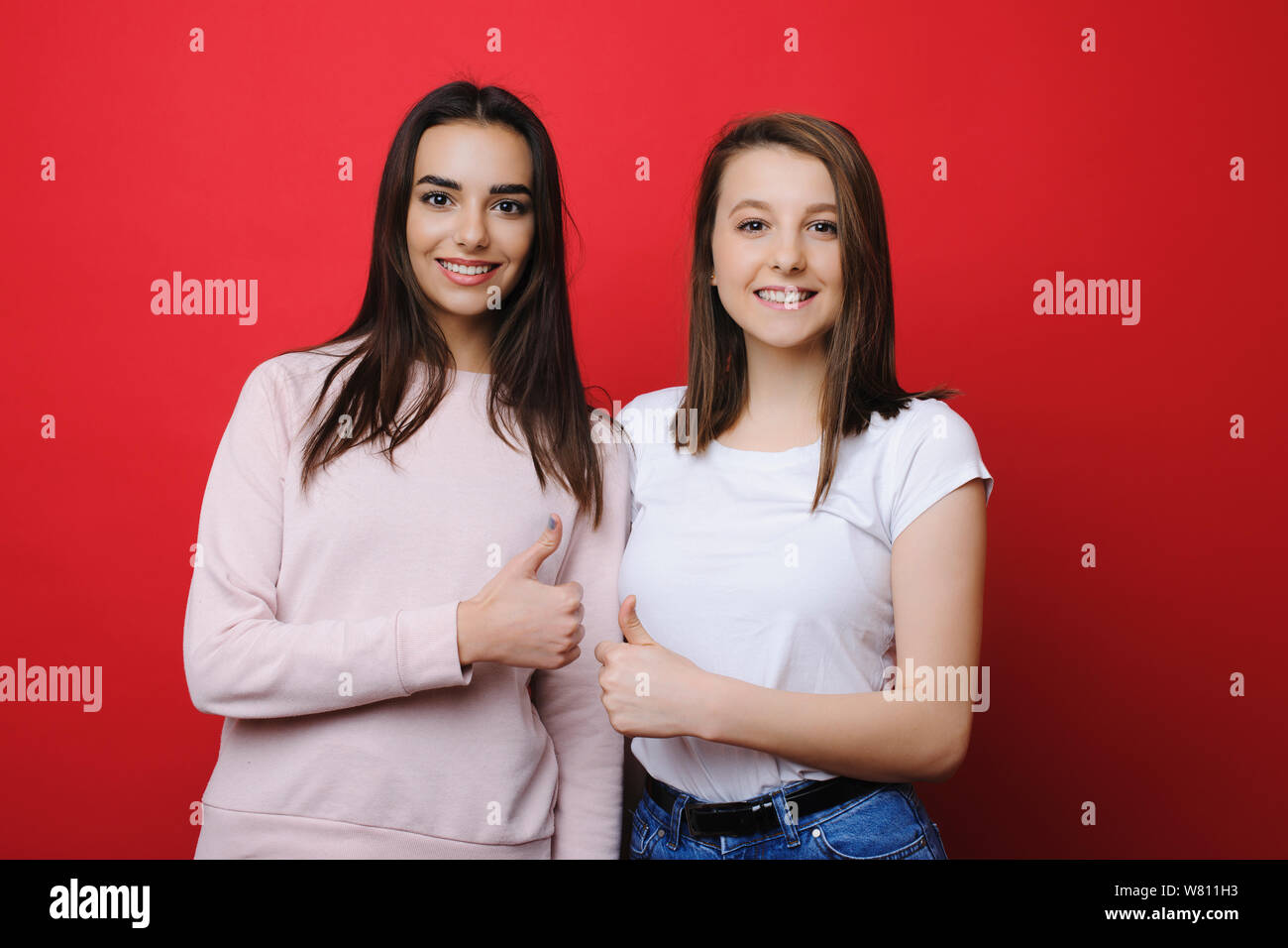 Portrait de deux meilleures amies filles habillés en vêtements décontractés à la caméra et en montrant que tout est bon smiling isolé sur fond rouge Banque D'Images