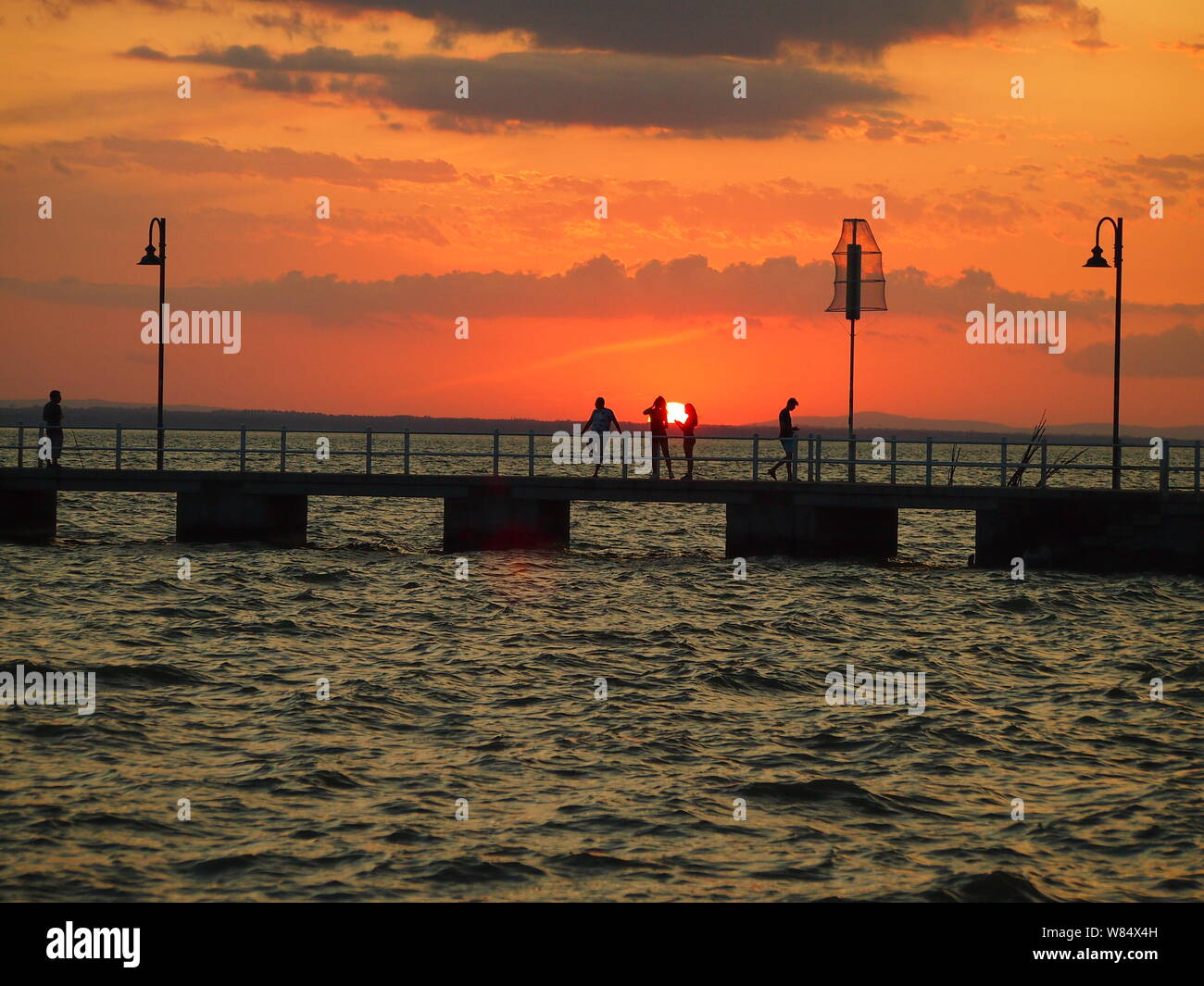 Personnes sur un quai silhouetted against orange ciel au coucher du soleil Banque D'Images