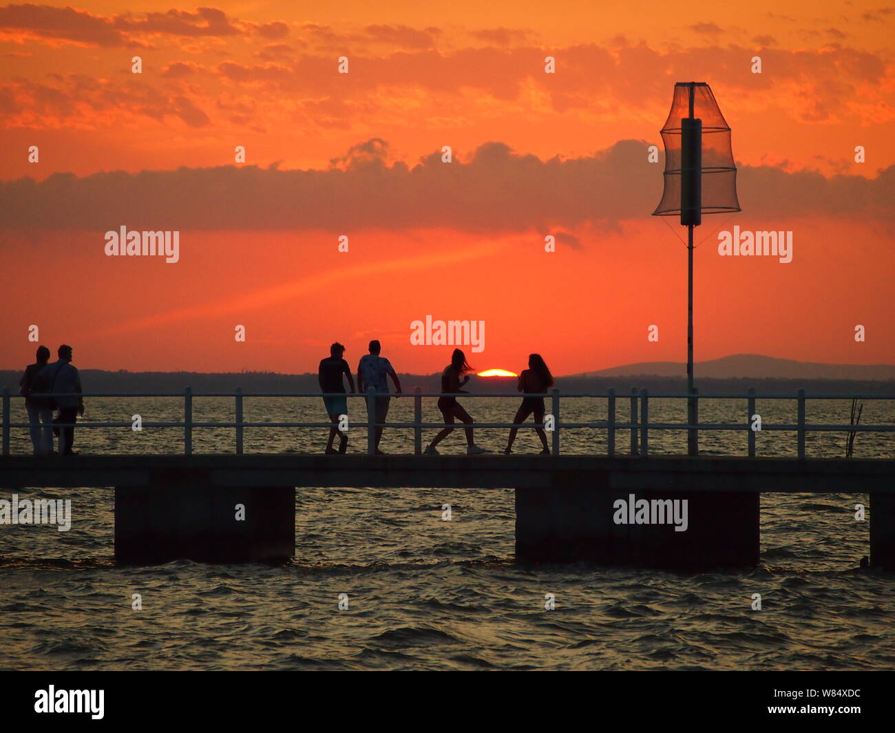 Personnes sur un quai silhouetted against orange ciel au coucher du soleil Banque D'Images