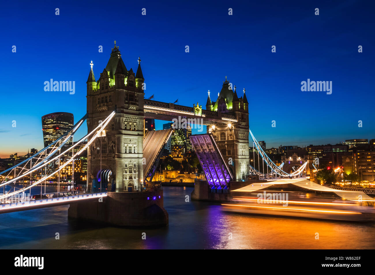 L'Angleterre, Londres, Tower Bridge ouverte la nuit avec voile en passant par la ville de London et à l'arrière Banque D'Images