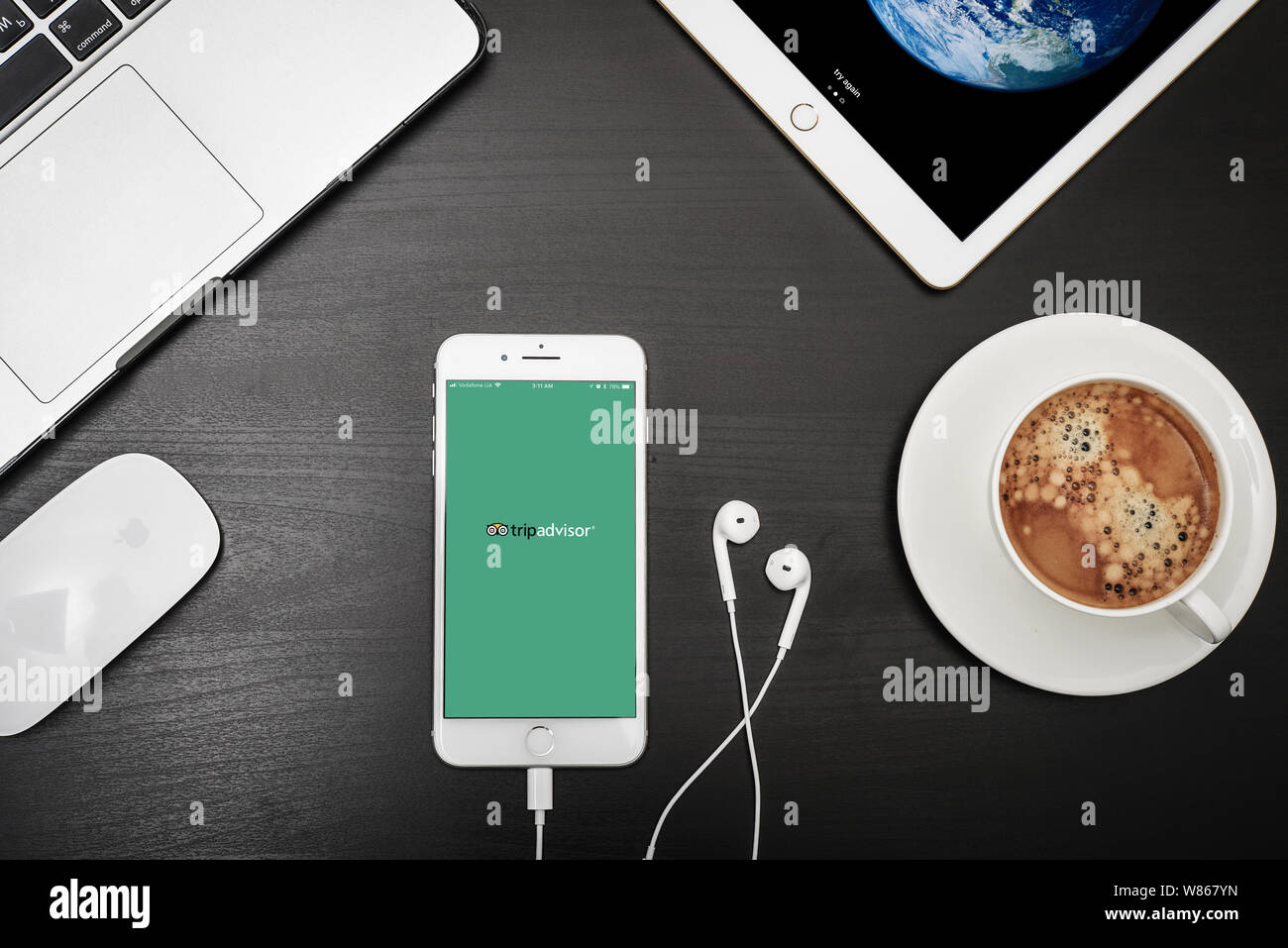 Kiev, Ukraine - Février 6, 2018 : Apple iPhone 8 plus avec Tripadvisor app sur l'écran avec macbook, ipad, café et casque sur bureau noir, haut Banque D'Images
