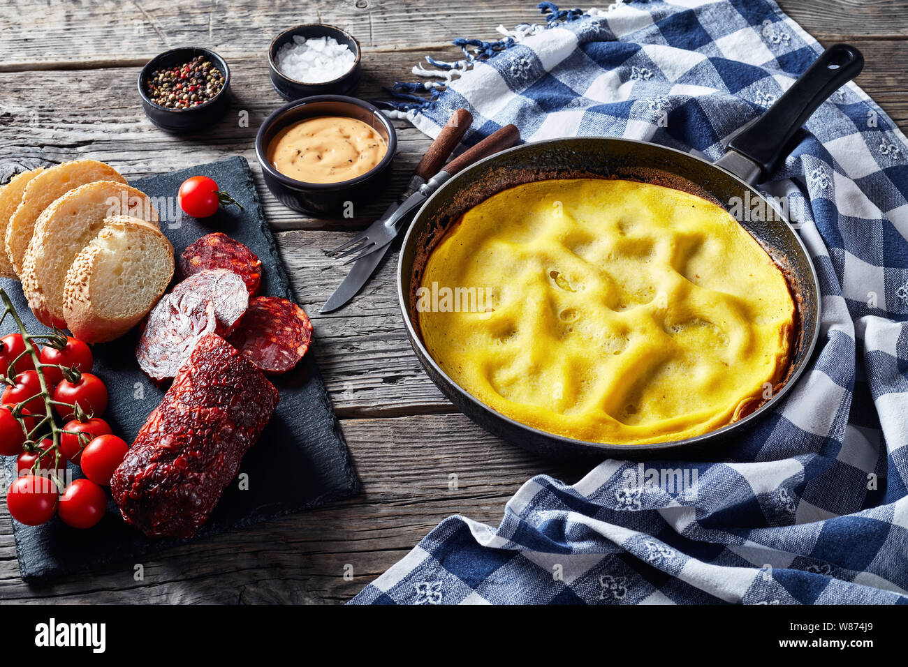 Omelette dans une poêle chaude, tranches de chorizo, pain et des tomates sur une liste de sélection sur une table en bois avec des serviettes de cuisine, vue de dessus, close-up Banque D'Images