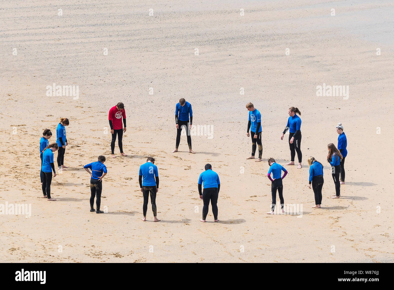 Les surfeurs débutants l'échauffement avant une leçon de surf sur une grande Gt. Plage de l'ouest à Newquay en Cornouailles. Banque D'Images