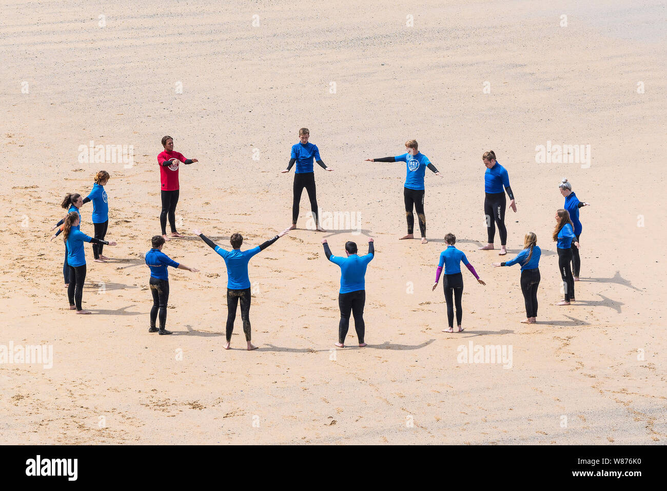 Les surfeurs débutants l'échauffement avant une leçon de surf sur une grande Gt. Plage de l'ouest à Newquay en Cornouailles. Banque D'Images