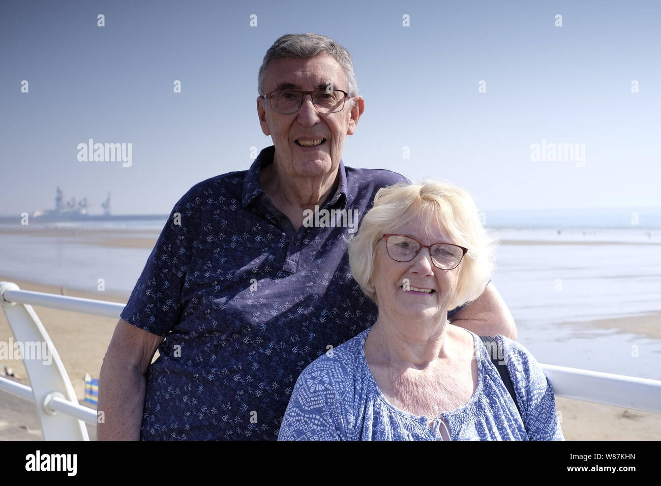 Un couple de personnes âgées à plus jeunes que leurs dernières années, à la recherche de l'appareil photo à la plage avec en arrière-plan Banque D'Images