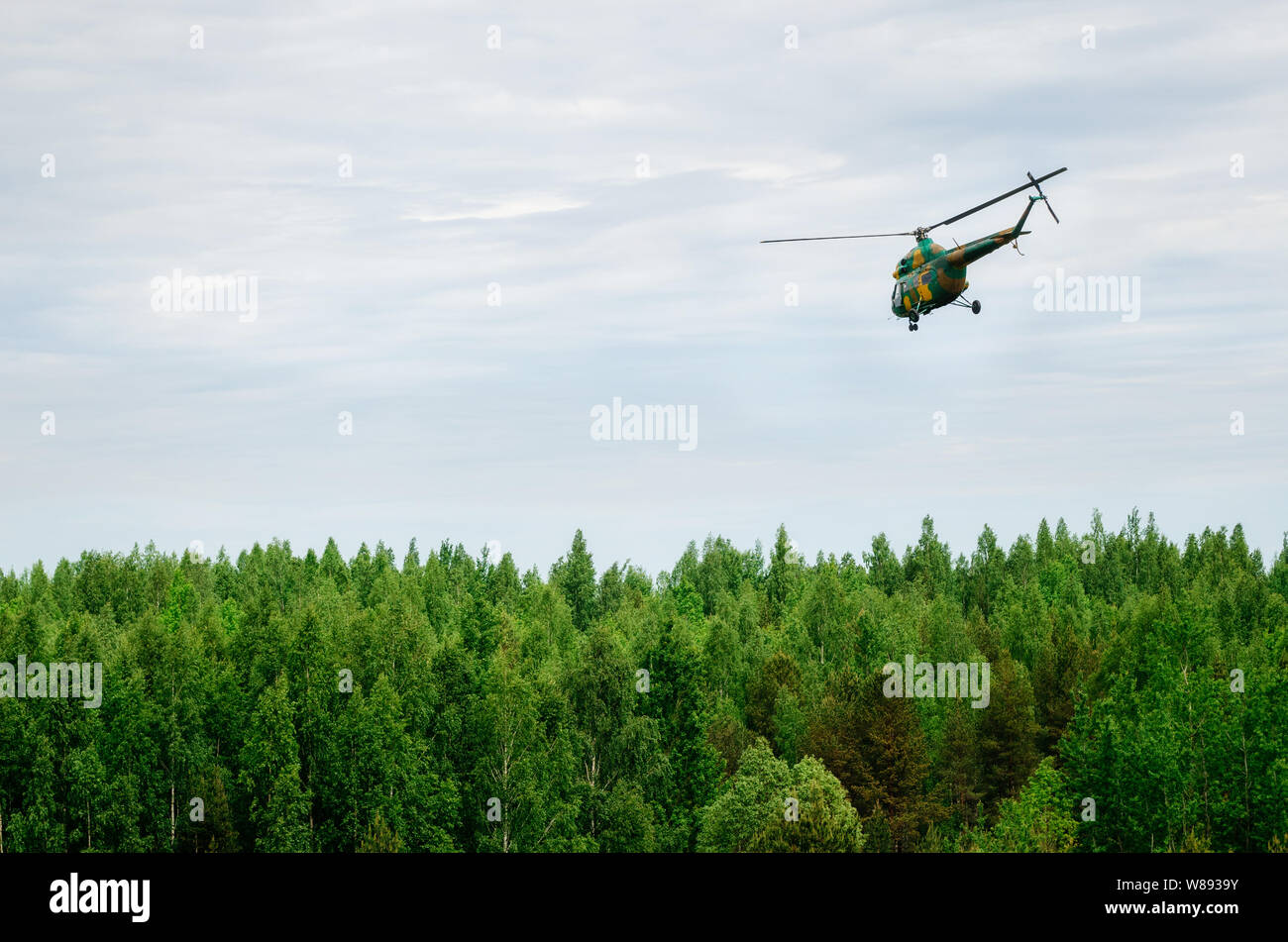 Hélicoptère de couleur kaki fait voler dans le ciel bleu au-dessus de Forest Banque D'Images