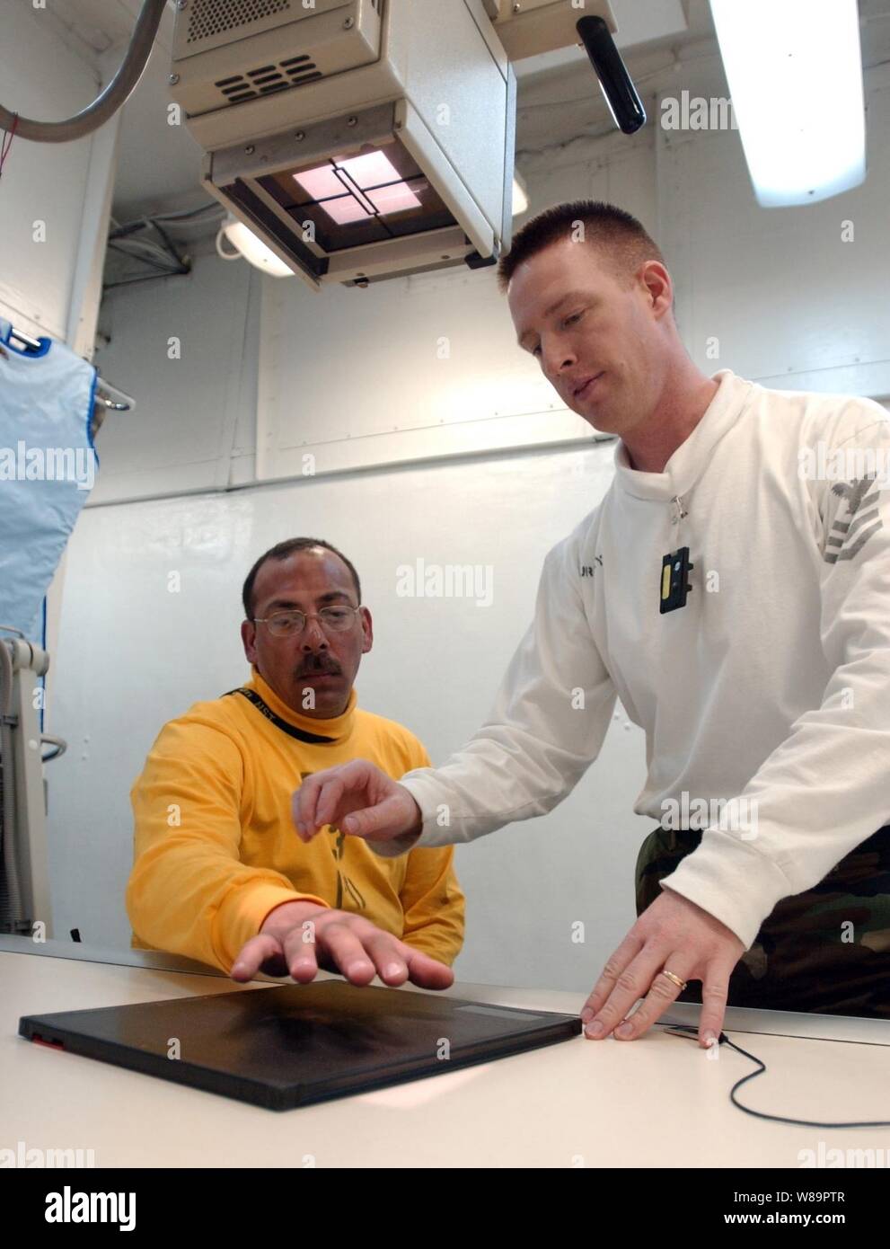 Le Maître de 1re classe de la marine Troy Murphy (à droite) prépare une main du patient pour un X-ray à bord du porte-avions USS Theodore Roosevelt (CVN 71) le 4 avril 2005. Murphy est une Marine hospital corpsman. Le porte-avions et son escadre aérienne de transporteur 8 sont actuellement en cours de formation dans l'océan Atlantique. Banque D'Images