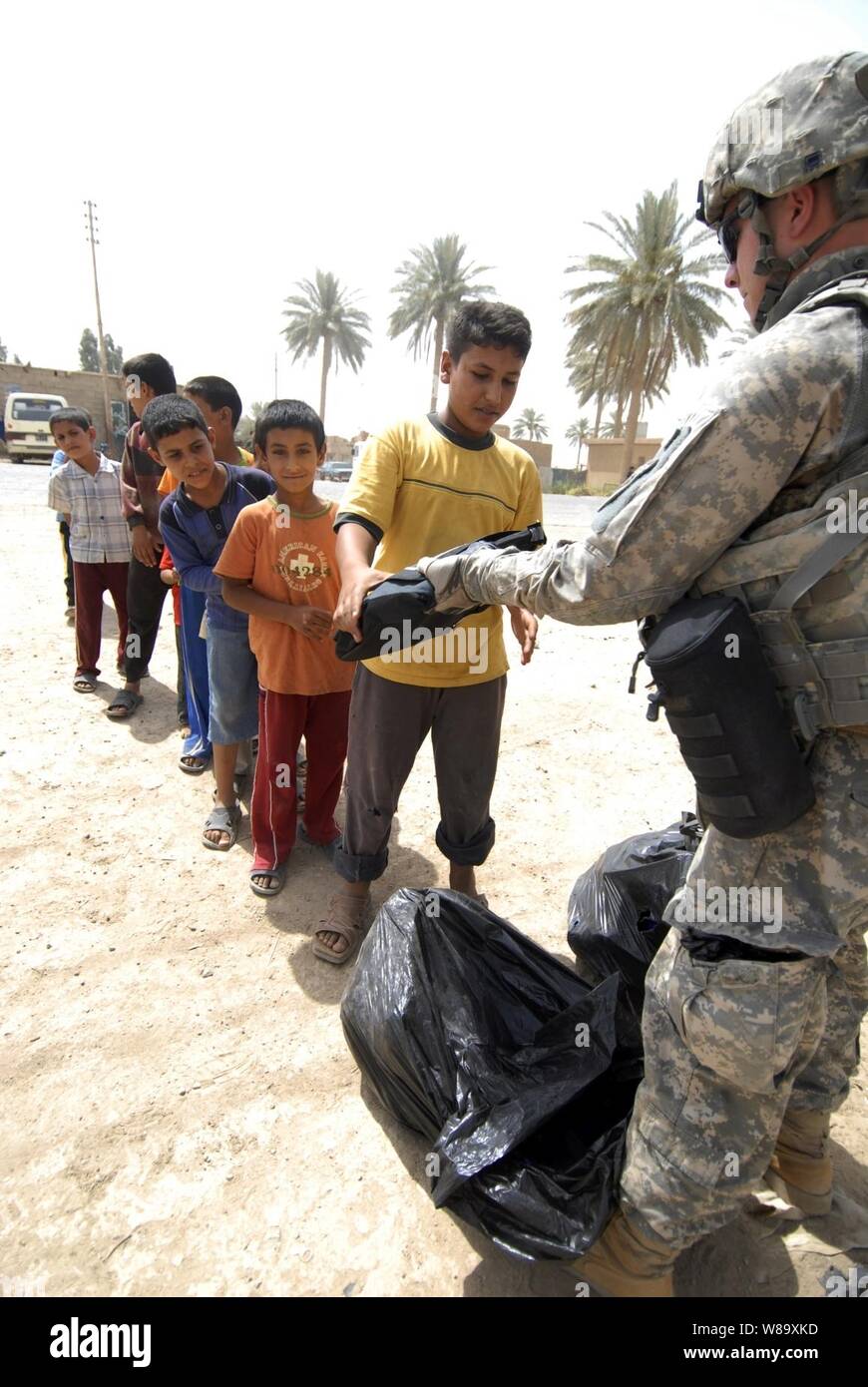 Un soldat de l'armée américaine avec le 1er Peloton, 1er Bataillon interarmes, 63e Régiment Blindé d'infanterie, 2e Brigade Combat Team lourd, 1re Division d'infanterie donne des sacs à dos remplis de fournitures scolaires aux enfants iraquiens dans Zaidon marché, hors de Bagdad, l'Iraq, le 23 juillet 2009. Banque D'Images
