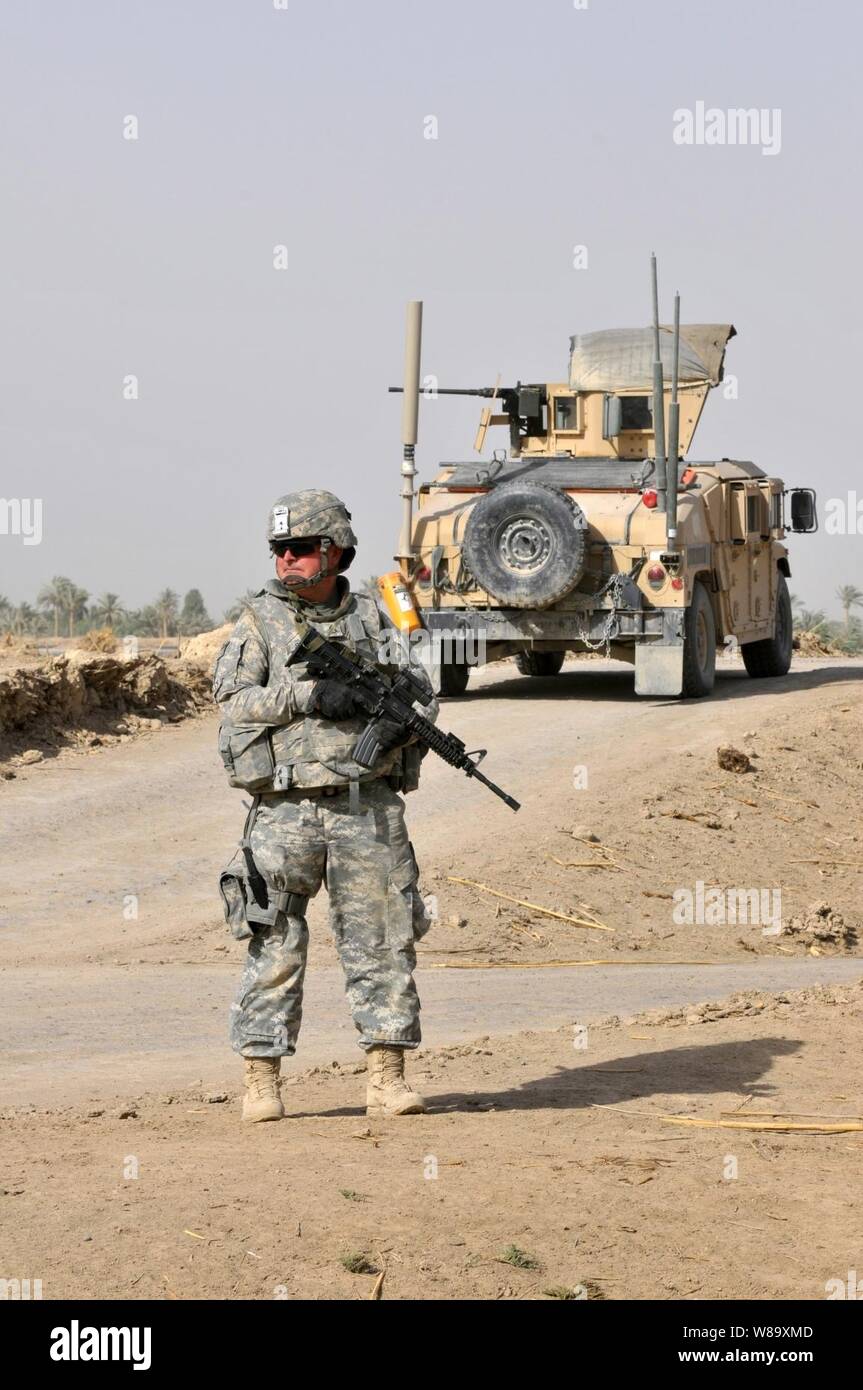 Un soldat de l'armée américaine avec le 1er Peloton, Comanche Troop, 1er escadron, 150e régiment de cavalerie lourde, 30e Brigade Combat Team, 1re Division de cavalerie fournit la sécurité comme des soldats iraquiens avec 1ère compagnie, 3e Bataillon, 23e Brigade, 17e Division irakienne conduite cache d'armes recherche dans les champs ouverts dans la zone à l'extérieur de Radwaniyah Bagdad, l'Iraq, le 18 juillet 2009. Banque D'Images