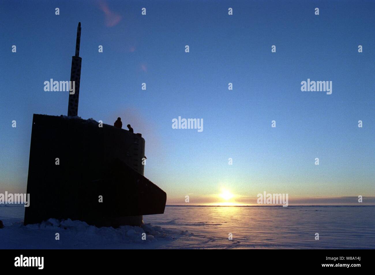 Deux membres de l'équipage de sous-marin d'attaque de l'USS Pogy (SSN 647) l'enquête entourant la glace après le lever du soleil à surface sous le biais d'une épaisse couche de 6 pouces de glace de l'Arctique. Le sous-marin est sur une mission de recherche de 45 jours au Pôle Nord. Sept conseillers techniques et scientifiques sont la réalisation d'expériences et de recueillir des échantillons pour des études dans les propriétés d'une masse d'eau, de la géophysique, de la mécanique et de la détection de la pollution dans l'océan Arctique. Le voyage de recherche est la deuxième des cinq déploiements prévus tout au long de l'année 2000. Banque D'Images