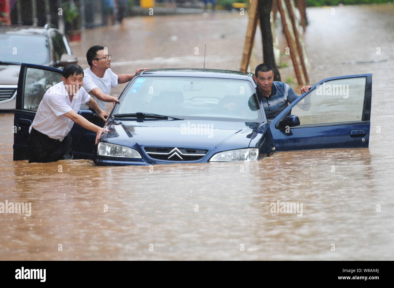 Les résidents locaux chinois poussent leur voiture sur une route inondée causées par de fortes pluies dans la ville de Jiujiang, province de Jiangxi, Chine orientale, le 15 juin 2016. R lourd Banque D'Images