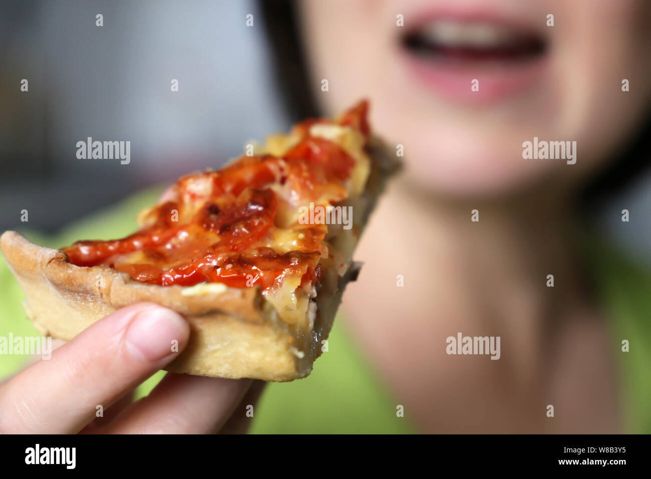 Girl eating et profiter de la pizza. Appétissant morceau de tarte avec le fromage, la viande et les tomates dans la main féminine close-up Banque D'Images