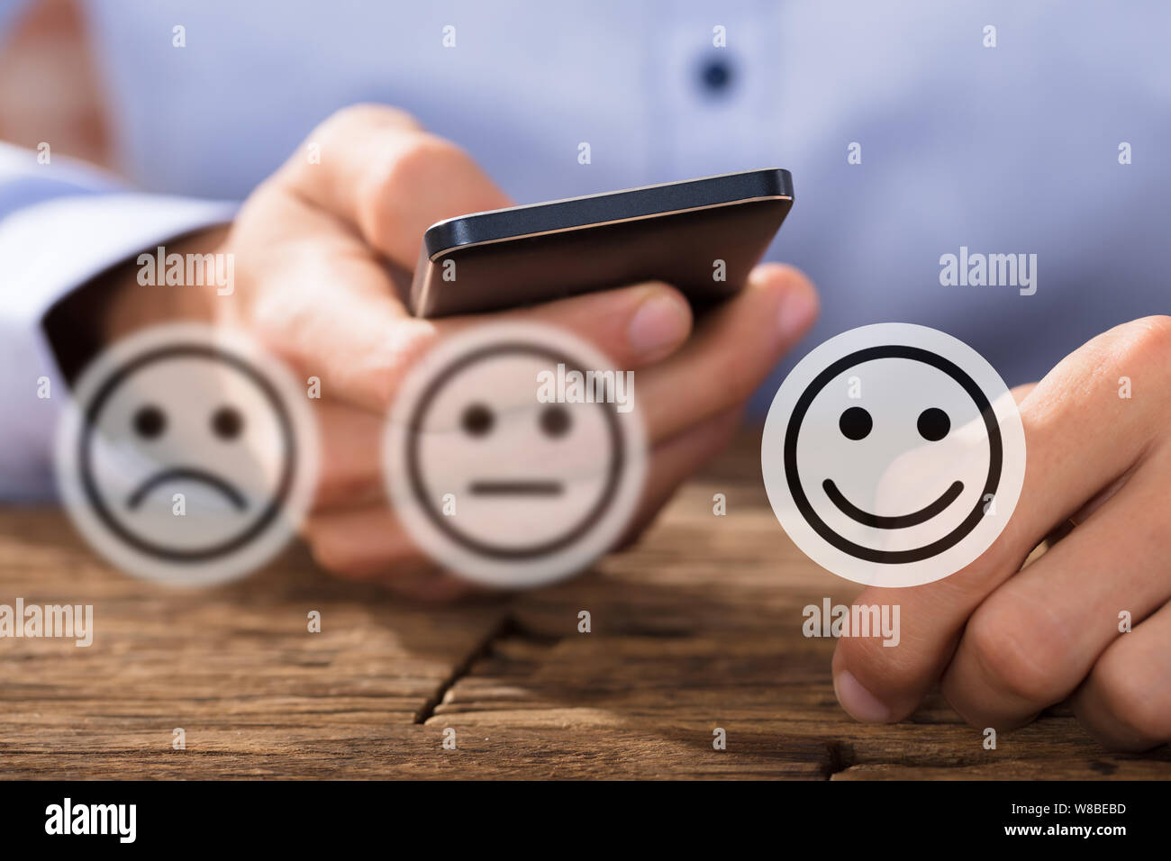 Expressions montrant les icônes en face de l'homme à l'aide d'un bureau en bois sur Mobilephone Banque D'Images