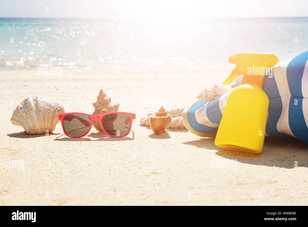 Lunettes de soleil en face de coquillage près de sac à main et jaune flacon pulvérisateur sur Sand At Beach Banque D'Images